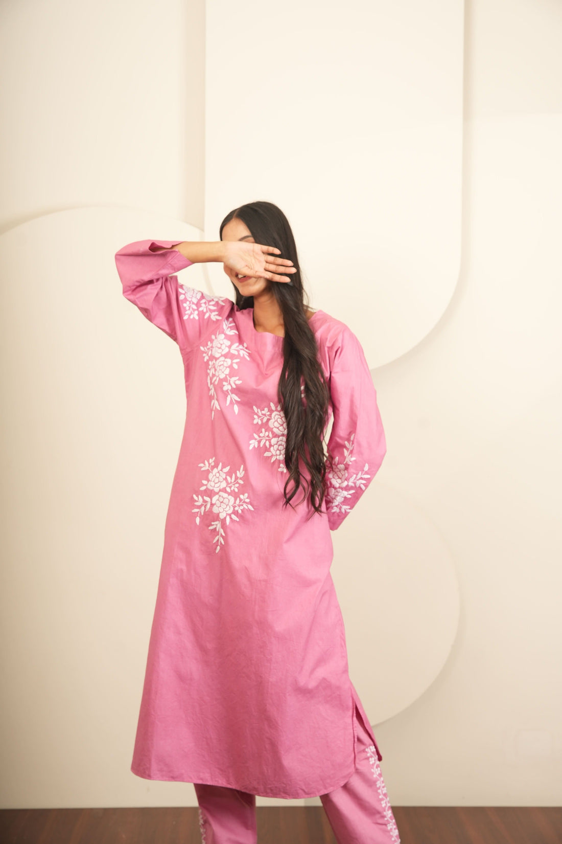 Person wearing a pink dress with white floral patterns on a white background