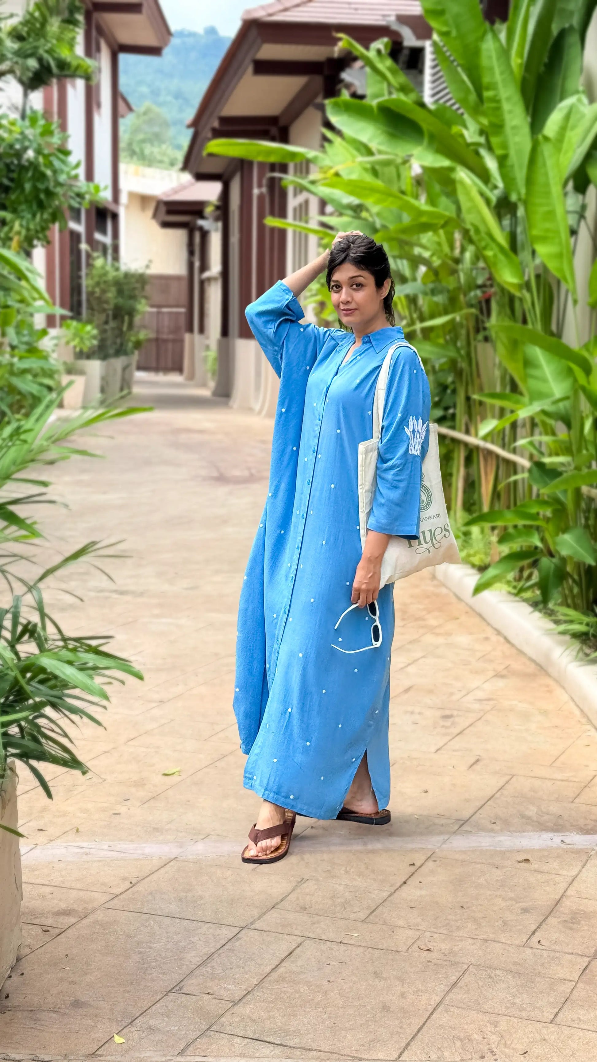 Woman in a blue dress standing on a pathway with greenery around